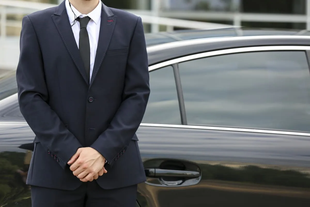 Agent de protection rapprochée en costume devant une berline
